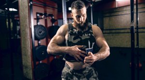 Bearded bodybuilder putting on a weighted vest in an empty gym