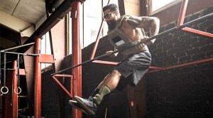 Muscular man with a beard and wearing glasses pulling himself up over a pull bar while wearing a weighted vest for his weekend workout