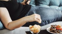 Женщина с избыточным весом ест нездоровую пищу на диване