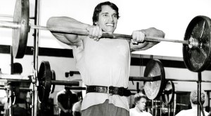 Arnold Schwarzeneggar working out doing an upright barbell row exercise