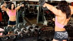 Professional female bodybuilder Alina Popa doing an arm workout with dumbbell raise exercise while looking in the mirror at the gym