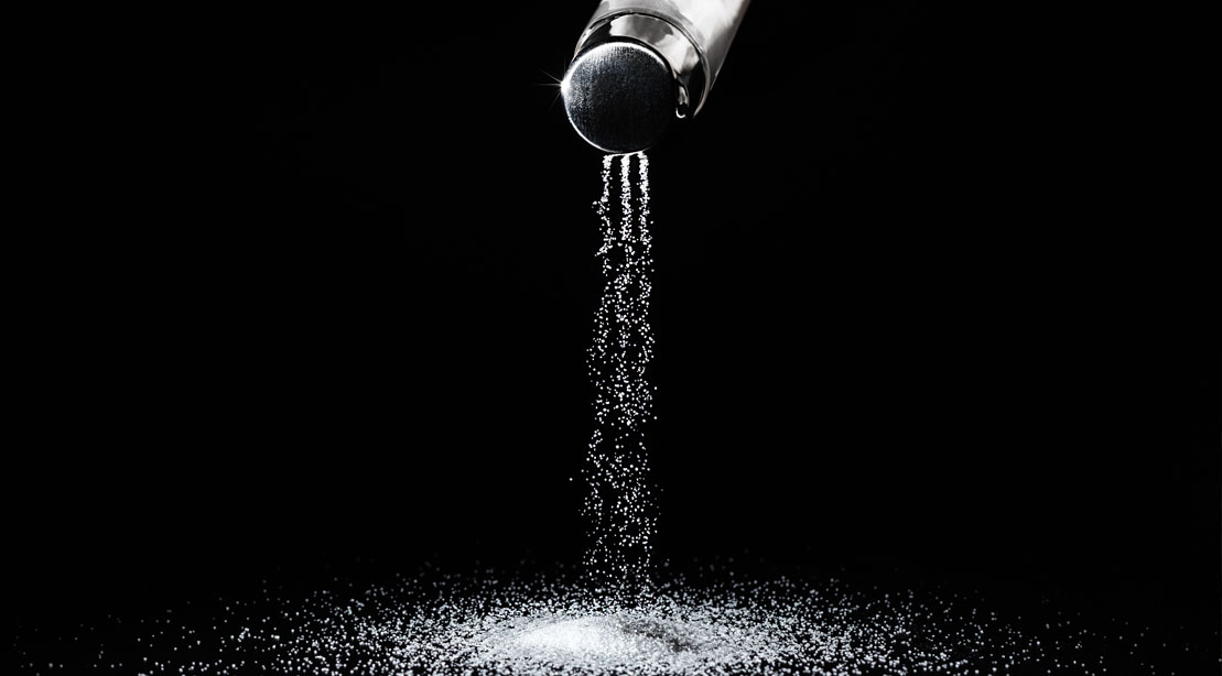 Sodium being poured from a salt shaker onto a black table