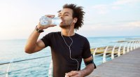 Black runner drinks a bottle of water as a good running tip and avoids dehydration