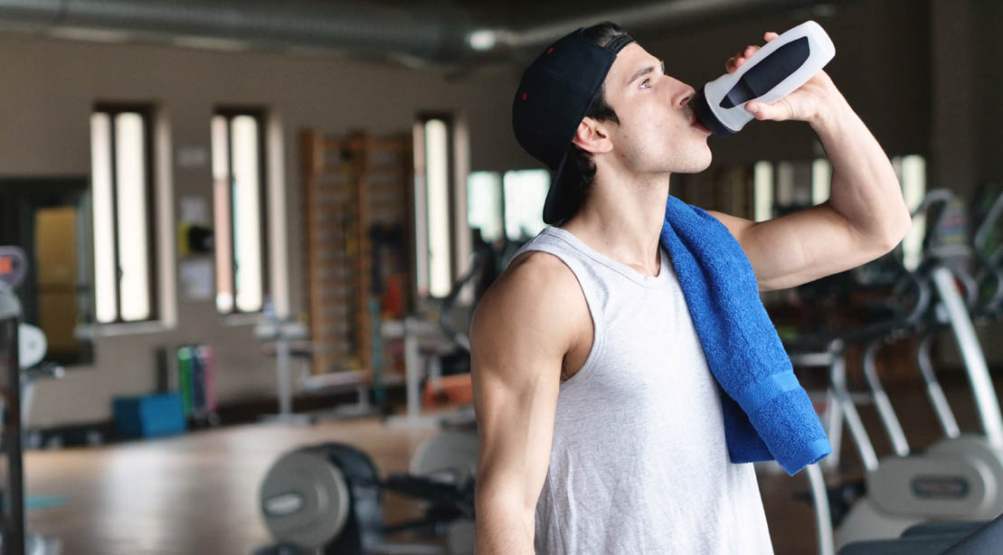 Physically fit man wearing a hat while drinking water and hydration drinks after working out