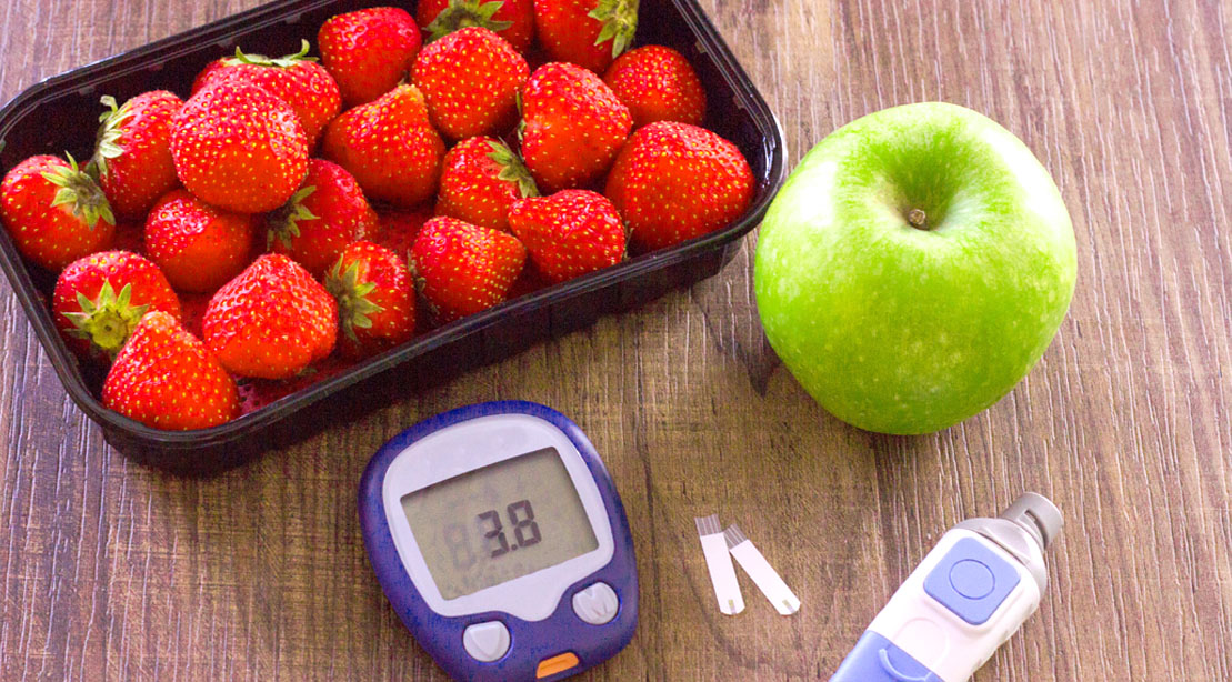 An apple and ripe strawberries and a glucometer used to monitor blood sugar