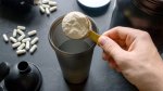 Protein powder in a scooper being poured into a protein shaker bottle