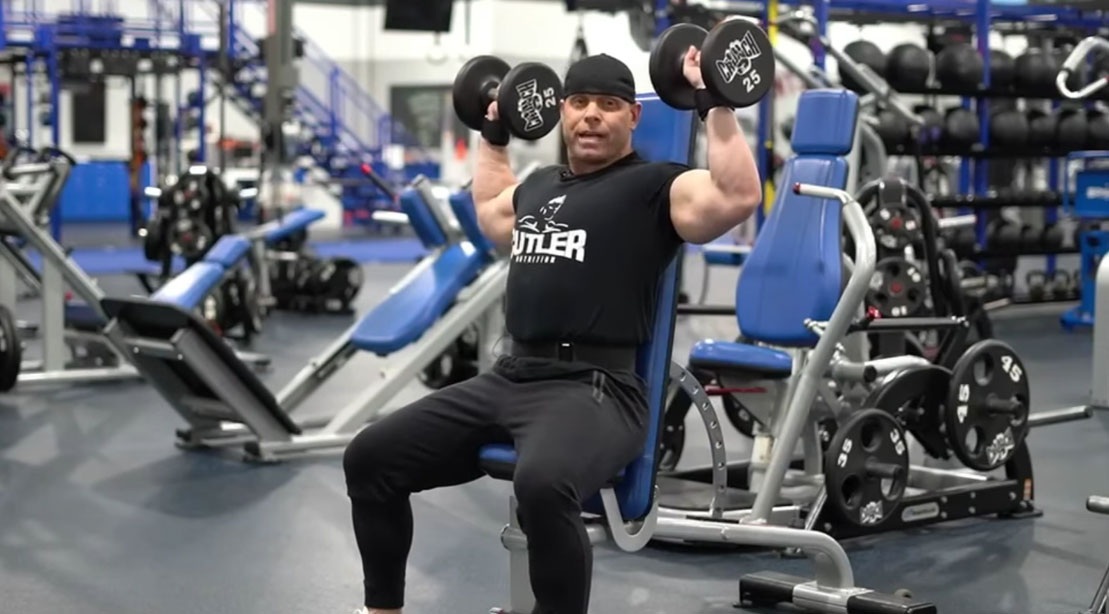 Former NPC bodybuilder David Baye showing how to do a seated dumbbell press exercise