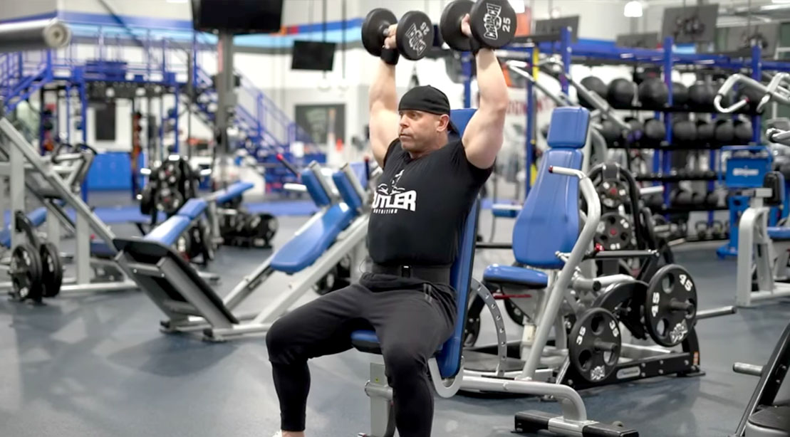 Former NPC bodybuilder David Baye showing how to do a seated dumbbell press exercise