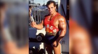 Bodybuilding legend Franco Columbu posing in front of dumbbell rack