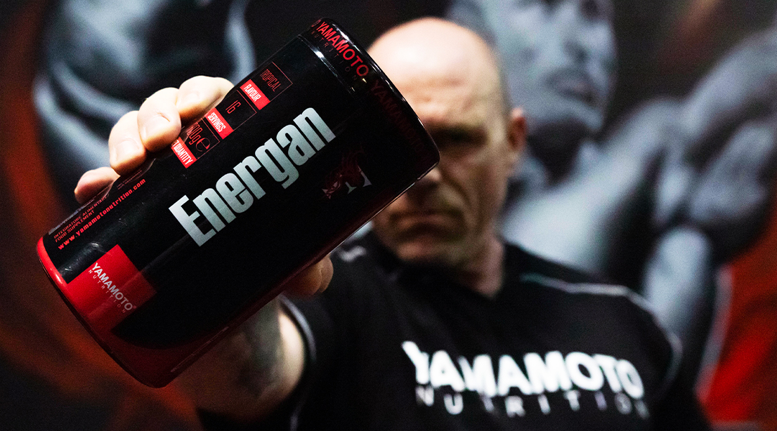 Male bodybuilder holding out a bottle of Energan and wearing a Yamamato Nutrition shirt