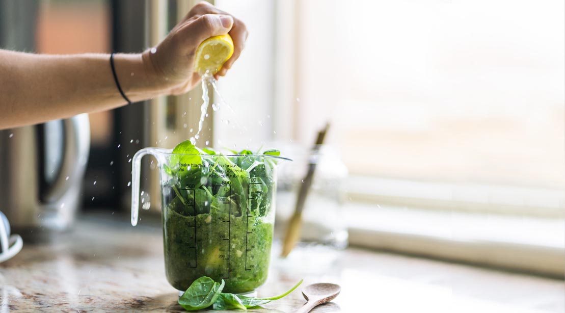 Woman making a healthy workout smoothie using spinach and lemon in a blender