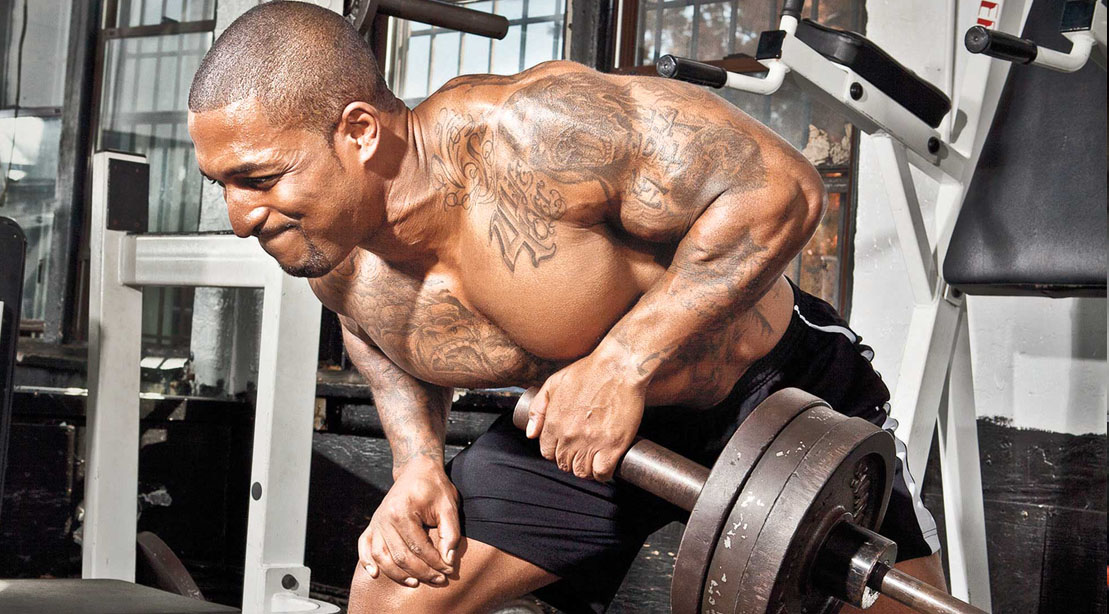 Black bodybuilder performing a full body workout with a unilateral row exercises such as a meadows row exercise