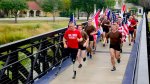 Military veteran Rob Jones running with running prosthetic legs running across a bridge with multiple flag carriers