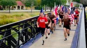 Military veteran Rob Jones running with running prosthetic legs running across a bridge with multiple flag carriers