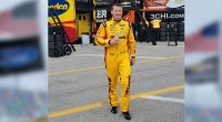 Nascar driver Michael McDowell drinking a can of soda wearing his race car uniform and walking on the track