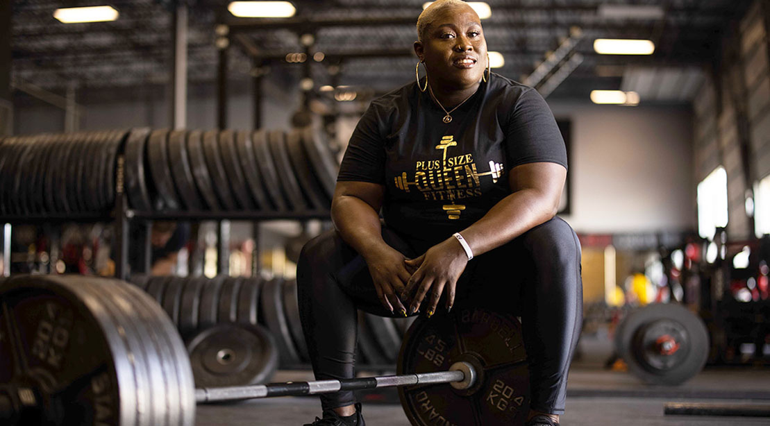 Tamara Walcott The Plus Size Fitness Queen and black female powerlifter sitting on a barbell in the gym