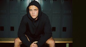 NCAA athlete sitting in the locker room wearing a black hoodie by BRADY clothing