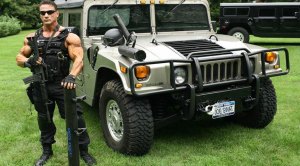 Police officer and security guard Joe Palumbo wearing a bullet proof vest and holding a gun in front of a hummer