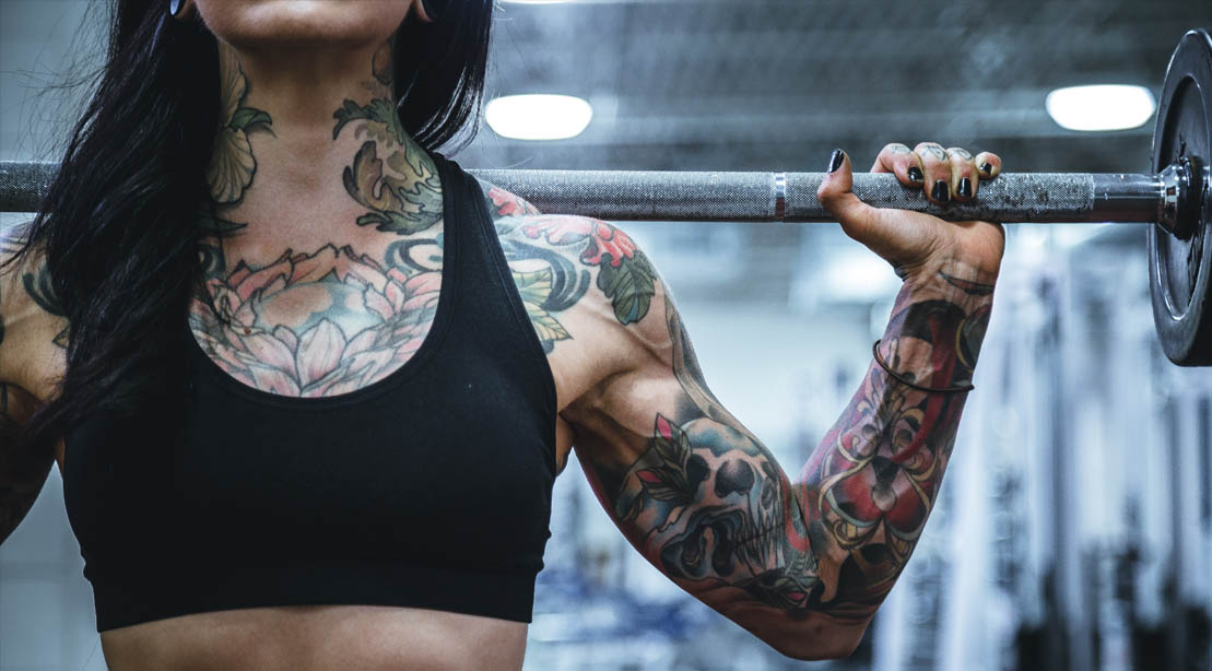 Tatooed fit female holding a barbell behind her neck to workout her neglected muscle groups
