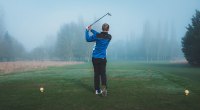 Golfer wearing a track suit playing golf on a foggy day increasing his chance of getting a golfing injury