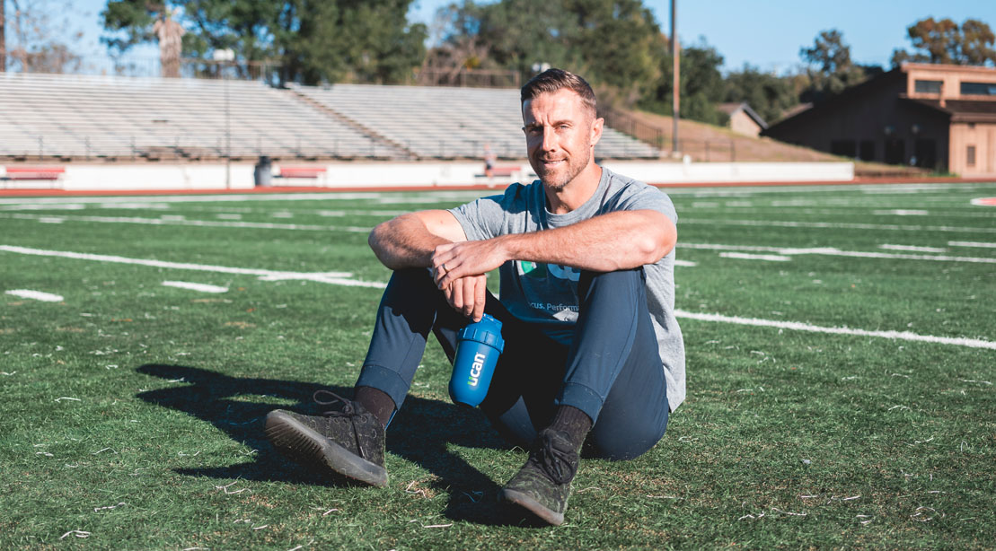 NFL Defensive Player of the Year Alex Smith sitting on the football field holding a UCAN protein shaker