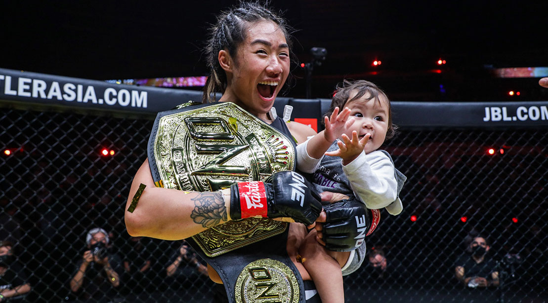 Unstoppable Angela Lee holding the One atomweight championship belt and her baby ava inside the MMA ring after winning a fight