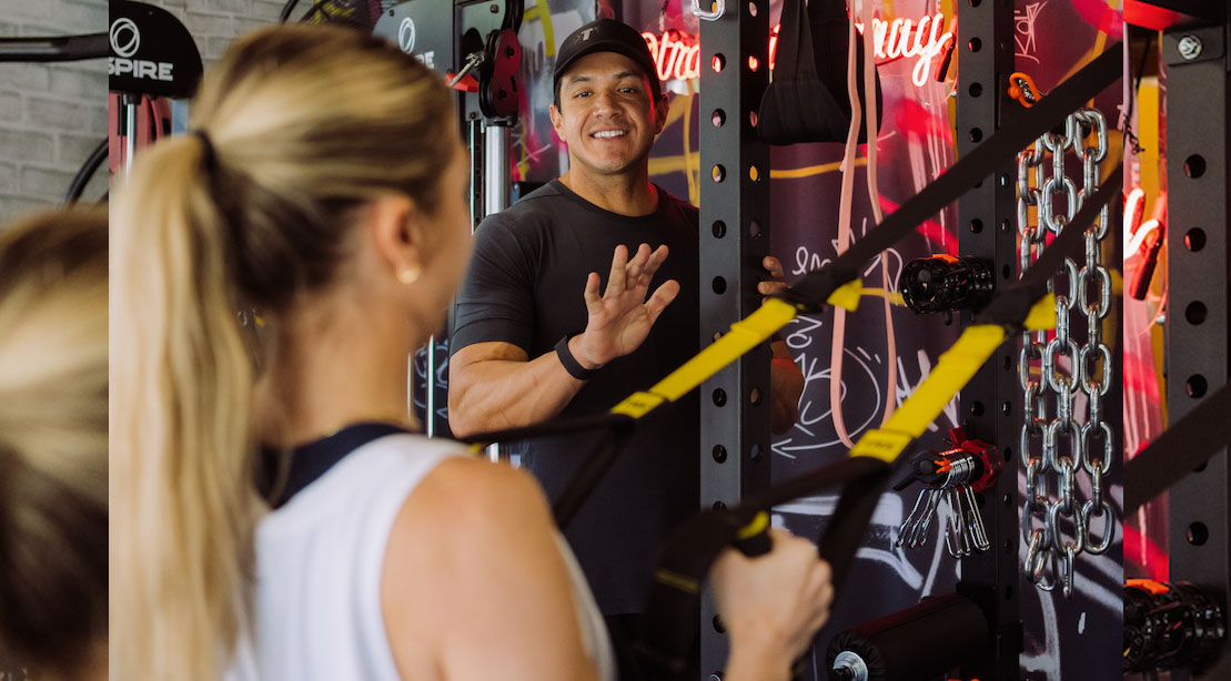 Personal Trainer Danny Saltos educating a client on metabolic health as she does a trx workout