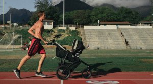 Physically fit father running a track while pushing a stroller