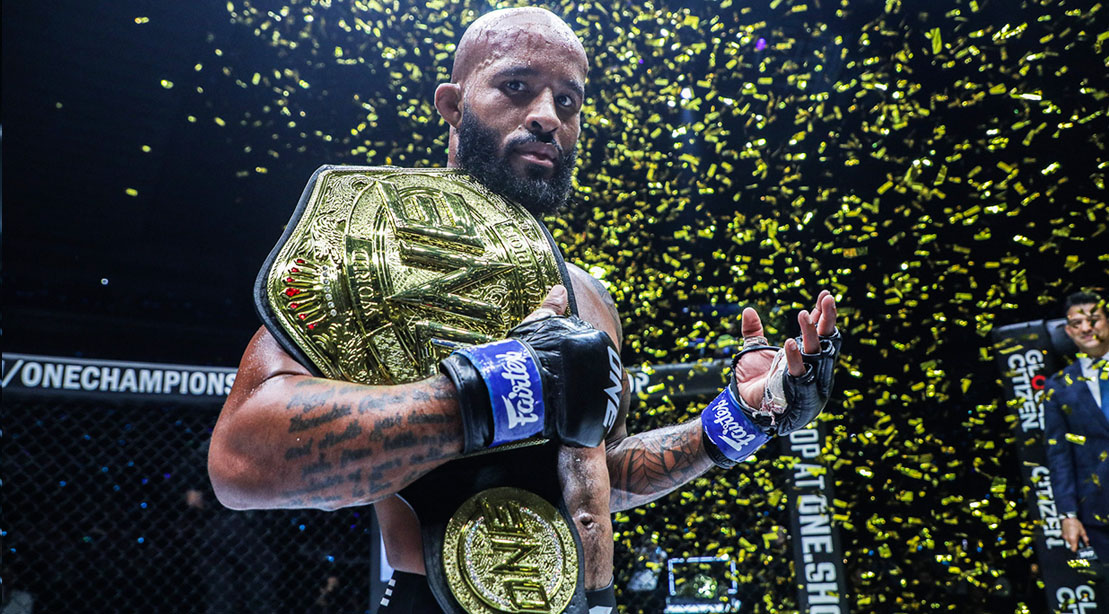 MMA fighter Demetrious Johnson holding a championship belt as confetti falls in the octagon