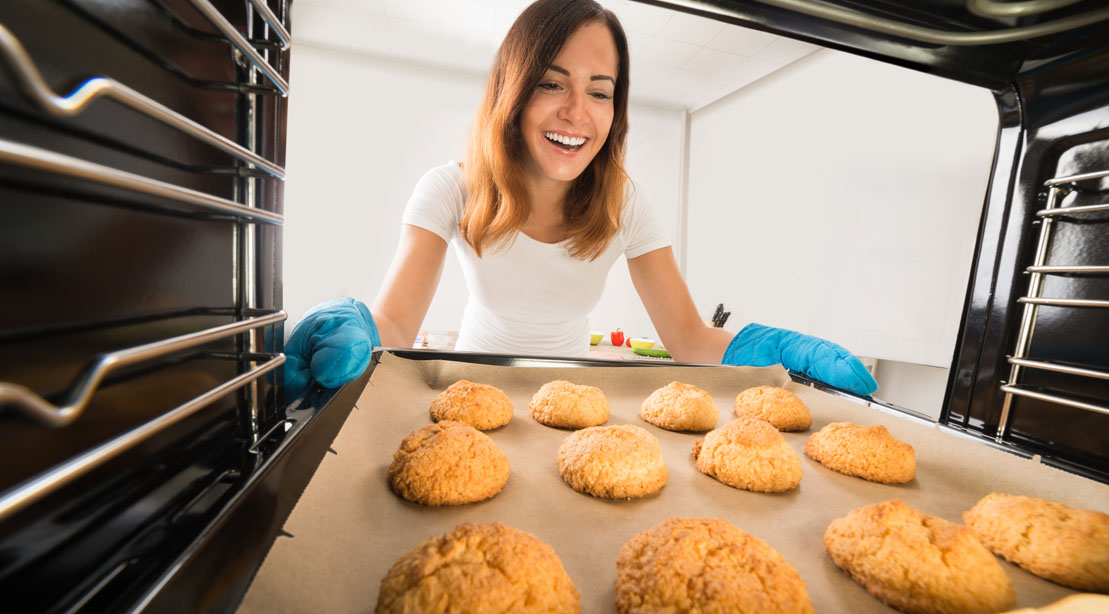 Happy young woman taking out her healthy holiday cookie dessert recipes from the oven