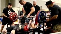 Fit bodybuilder performing heavy bench press with observers