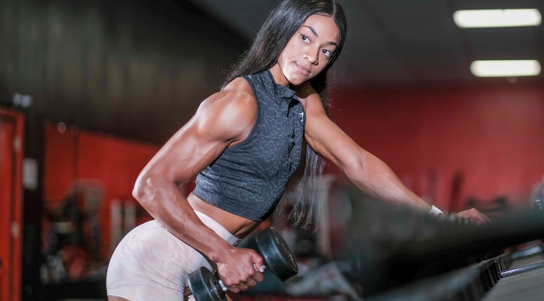 Erica Evans lifting a light weight dumbbell at the dumbbell rack