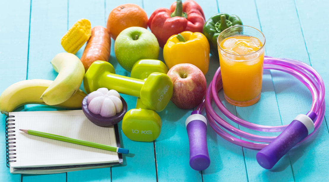 Healthy fruits and vegetables on a blue table next to a note pad