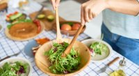 Woman making a perfect salad with vegetables and dressing and mixing it up in a wooden bowl