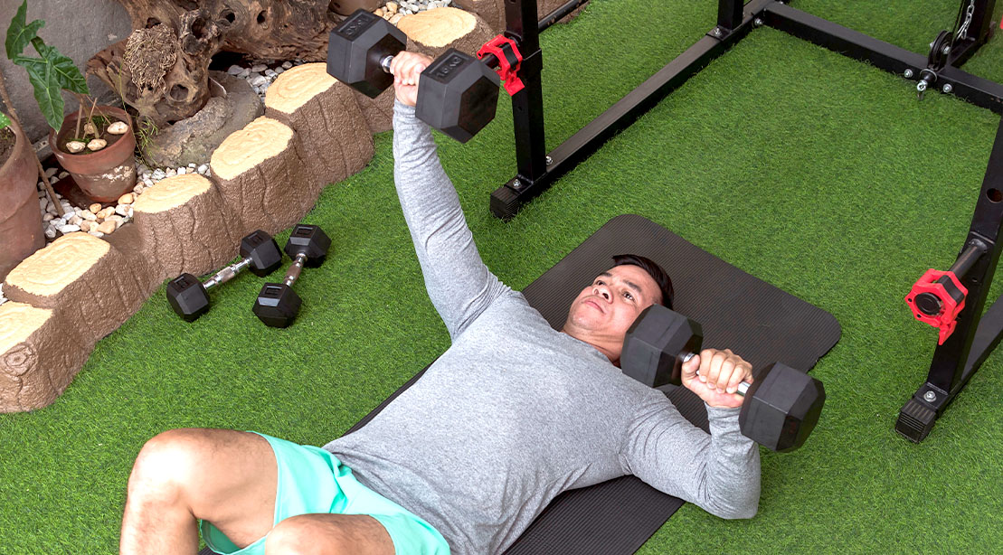 Fit man performing a unilateral dumbbell floor press