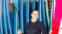 Female holding a paddleboard and paddle while wearing a wetsuit