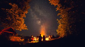 Couple camping outdoors with a group hanging by the fire underneath the stars
