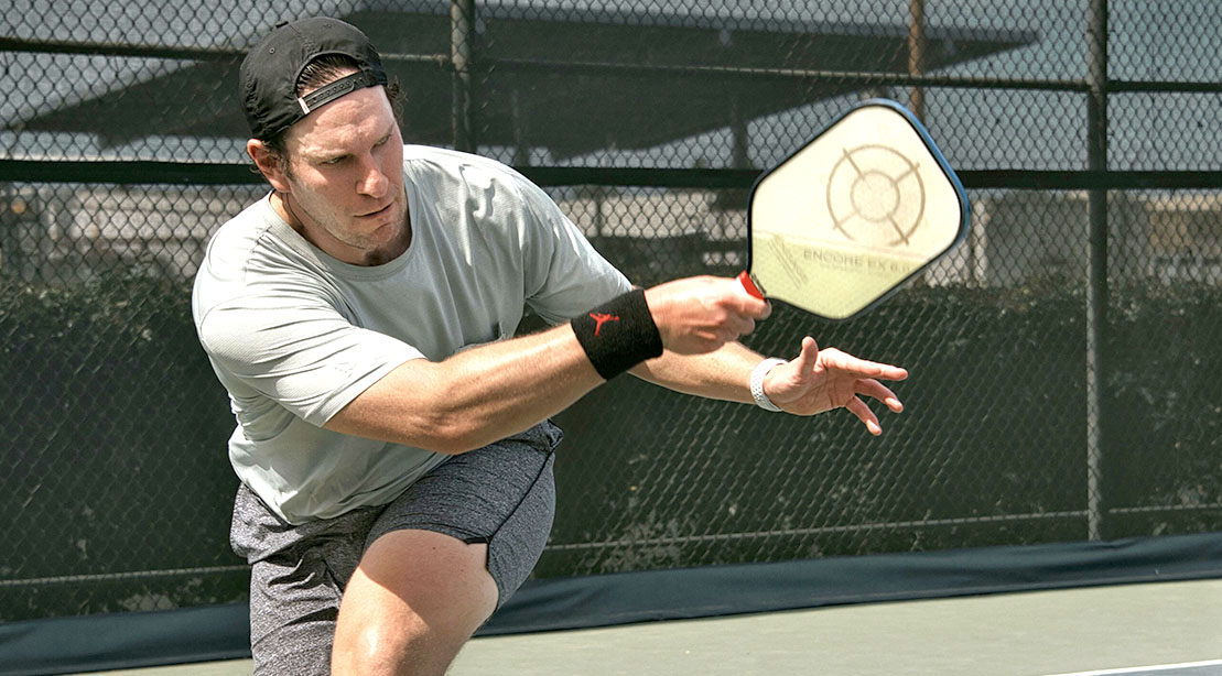 Pickleball player squatting over to hit the pickleball