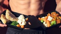 FIt man with six pack abs holding containers of healthy food and vegetables